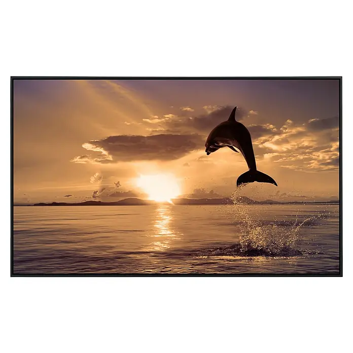 Papermoon Infrarot-Bildheizkörper Springender Delfin - 90 x 50 cm, 450 W - Ein gerahmtes Foto eines springenden Delfins vor einem orangefarbenen Sonnenuntergang. Die Leinwand verleiht dem Bild eine künstlerische Tiefe.