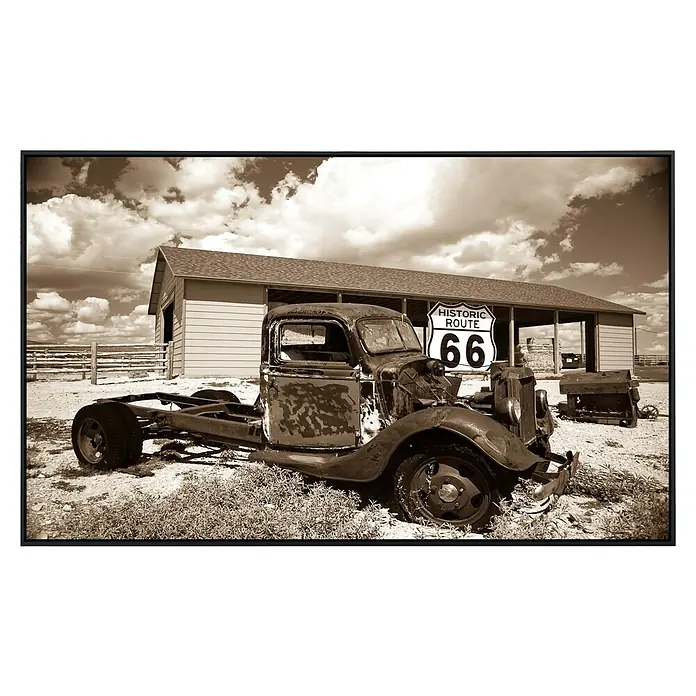 Papermoon Infrarot-Bildheizkörper Rosty Truck - 100 x 60 cm, 600 W - Ein verrosteter Oldtimer-LKW steht vor einem Route 66-Schild, eine nostalgische Darstellung amerikanischer Geschichte und Verfalls.
