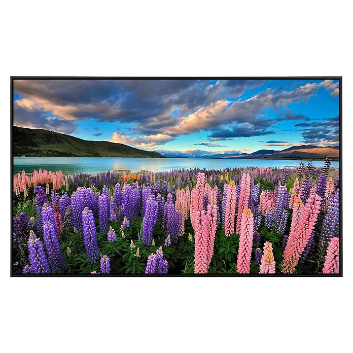 Papermoon Infrarot-Bildheizkörper See Tekapo Lupinen - 120 x 60 cm, 1.200 W - Ein faszinierender Fernseher zeigt eine atemberaubende Landschaft mit blühenden Blumen und einem malerischen See unter einem bewölkten Himmel.