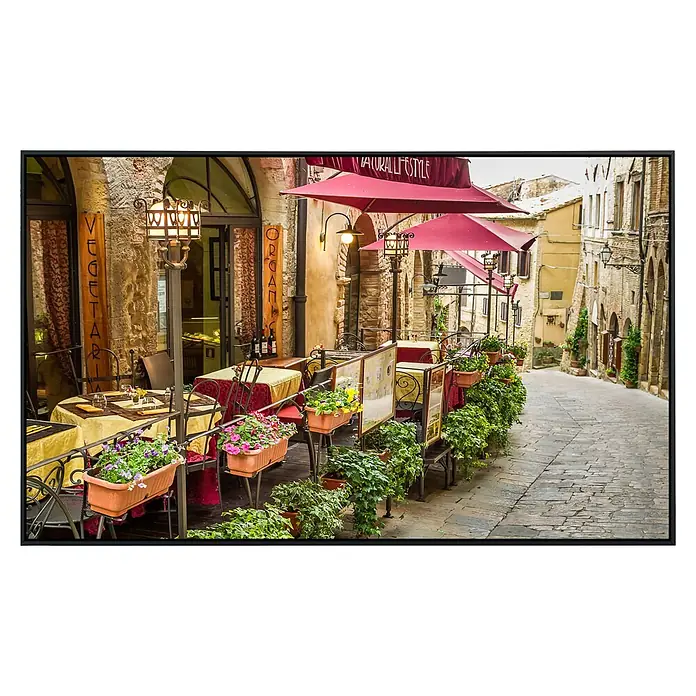 Papermoon Infrarot-Bildheizkörper Vintage Café - 120 x 60 cm, 1.200 W - Einladendes Straßencafé mit blumengeschmückten Tischen und roten Sonnenschirmen, das zum Verweilen einlädt. Dekorative Laternen beleuchten den Bereich.