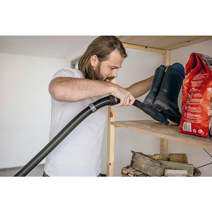 Kärcher Elektro-Nass- & Trockensauger WD 3 S V-17/4/20 - 1.000 W, Behältervolumen: 17 l - Mann saugt Staub mit Kärcher Staubsauger auf einem Regal mit Stiefeln und einer Tüte. Praktisch und effizient für die Reinigung.