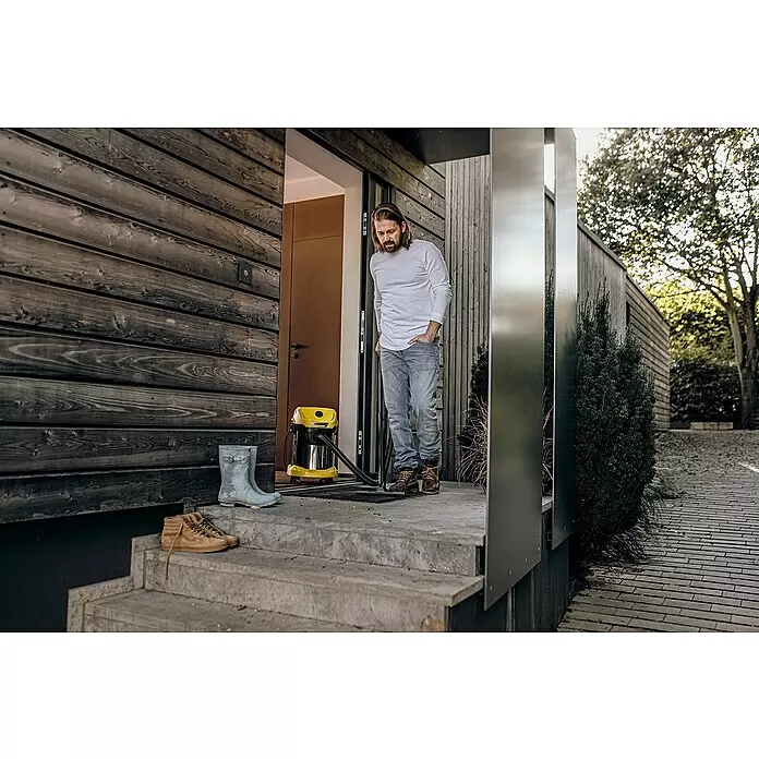 Kärcher Elektro-Nass- & Trockensauger WD 3 S V-17/4/20 - 1.000 W, Behältervolumen: 17 l - Gelber Kärcher Nass-/Trockensauger auf einer Fußmatte vor einem Hauseingang, mit einem Mann daneben.
