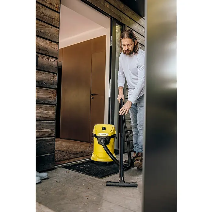 Kärcher Elektro-Nass- & Trockensauger WD 3 V-17/4/20 - 1.000 W, 17 l - Mann saugt mit einem gelben Kärcher Mehrzwecksauger eine Fußmatte vor einer Haustür.