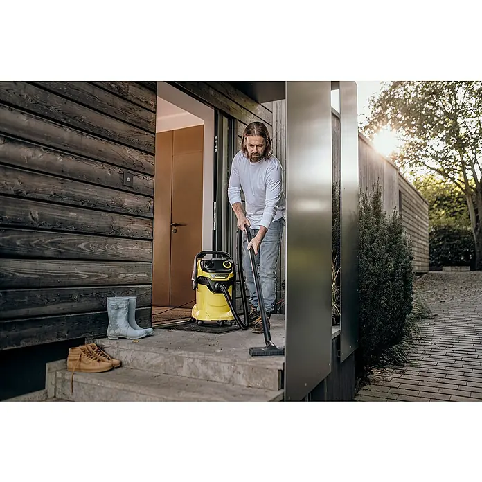 Kärcher Elektro-Nass- & Trockensauger WD 5 V-25/5/22 - 1.100 W, Behältervolumen: 25 l - Ein Mann benutzt einen gelben Kärcher Staubsauger auf einer Veranda. Der Kärcher Staubsauger ist das Hauptmerkmal des Bildes.