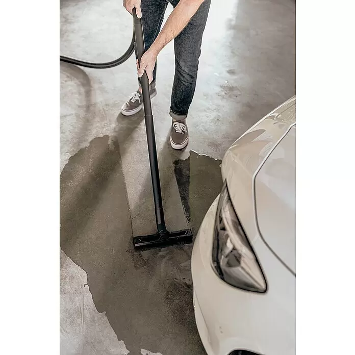 Kärcher Elektro-Nass- & Trockensauger WD 3 S V-17/4/20 - 1.000 W, Behältervolumen: 17 l - Eine Person saugt mit einem schwarzen Nass-/Trockensauger Wasser von einem Betonboden neben einem Auto.