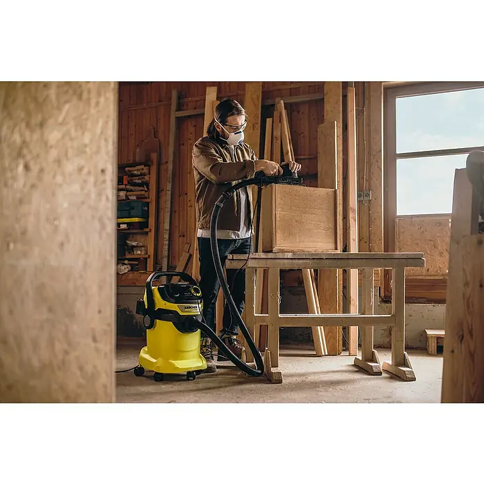 Kärcher Elektro-Nass- & Trockensauger WD 5 P V-25/5/22 - 1.100 W, 25 l - Mann schleift Holz mit einem Schleifer, verbunden mit einem gelben Kärcher Staubsauger, in einer Werkstatt.