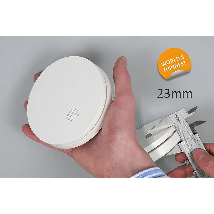 UniTEC Rauchwarnmelder Design - Durchmesser: 12,5 cm, Höhe: 2,5 mm, Alarmsignal: 85 dB, Weiß - Das Bild zeigt einen sehr dünnen, weißen Rauchmelder, der mit einer Schieblehre auf 23 mm gemessen wird. "World's Thinnest" Aufkleber.
