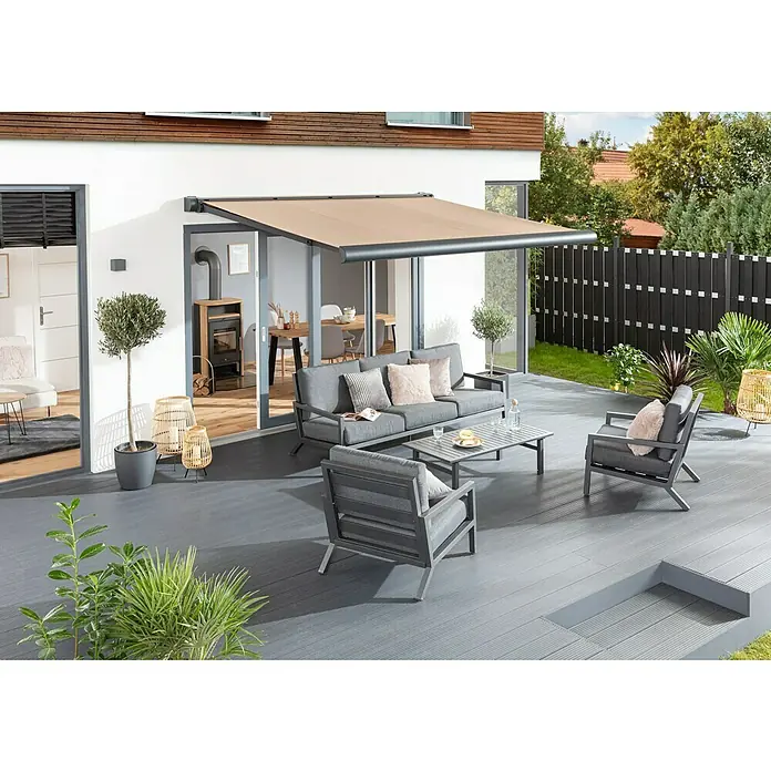 Sunfun Vollkassettenmarkise Elba - Beige, Farbe Gestell: Anthrazitgrau, Breite: 4 m, Ausfall: 3,5 m - Eine stilvolle Terrassenüberdachung bietet Schatten für eine moderne Lounge-Gruppe mit Sofa und Sesseln auf einer grauen Holzterrasse.