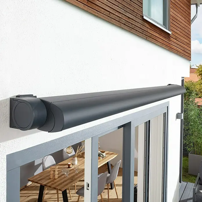 Sunfun Vollkassettenmarkise Elba - Grau, Farbe Gestell: Anthrazitgrau, Breite: 3 m, Ausfall: 2,5 m - Bild einer eleganten, grauen Kassettenmarkise, die an einer weißen Hauswand über einer Terrassentür montiert ist und Schatten spendet.