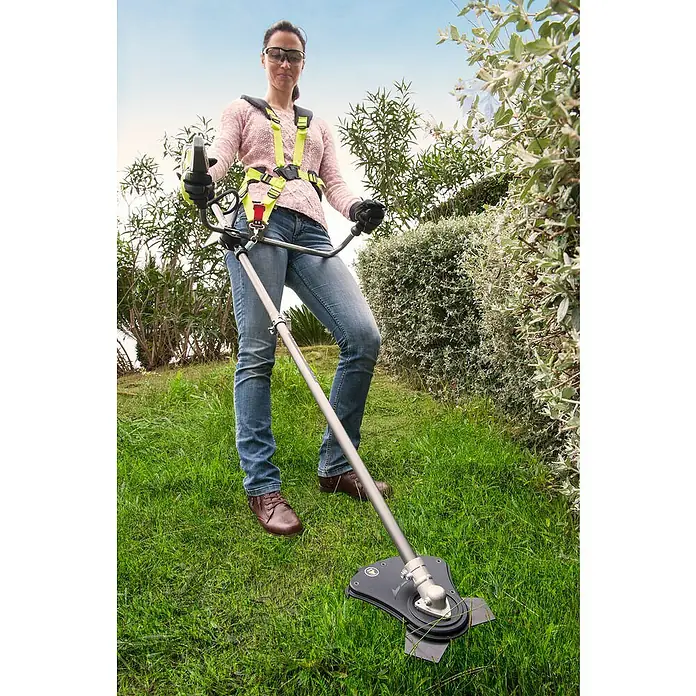 Ryobi ONE+ Akku-Rasentrimmer RBC 18X20B4F - 18 V, 4 Ah, Li-Ionen, 1 Akku, Schnittbreite Messer: 20 cm, Schnittbreite Faden: 30 cm - Eine Frau, die einen Rasentrimmer mit Tragegurt benutzt, um das Gras auf ihrem Rasen zu schneiden.