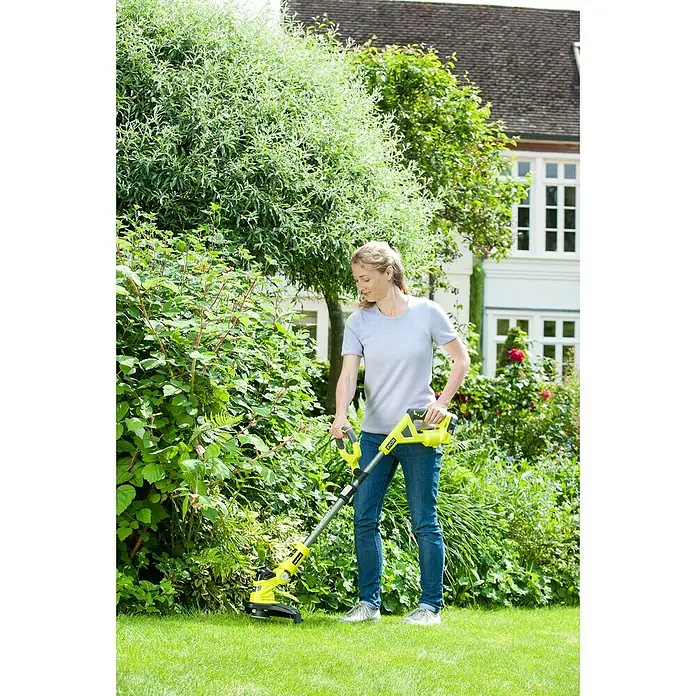 Ryobi ONE+ Hybrid-Rasentrimmer RLT1831H25F - 18 V, 2,5 Ah, Li-Ionen, 1 Akku - Frau benutzt einen gelben Ryobi-Rasentrimmer im Garten, um das Gras zu trimmen. Das Haus ist im Hintergrund.