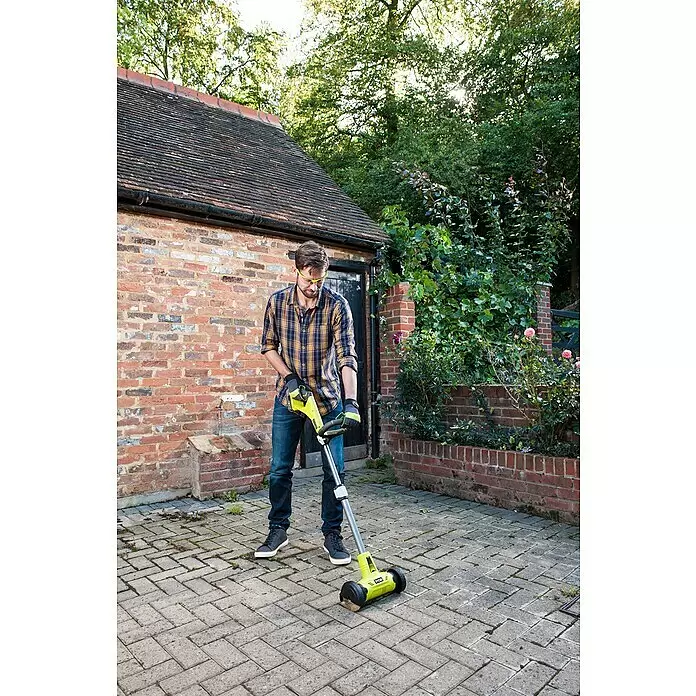 Ryobi ONE+ Limpiador de juntas de batería RY18PCA-0 - 18 V, Iones de litio, Sin batería - Hombre usa un cepillo para malas hierbas inalámbrico amarillo y negro para limpiar un camino pavimentado.