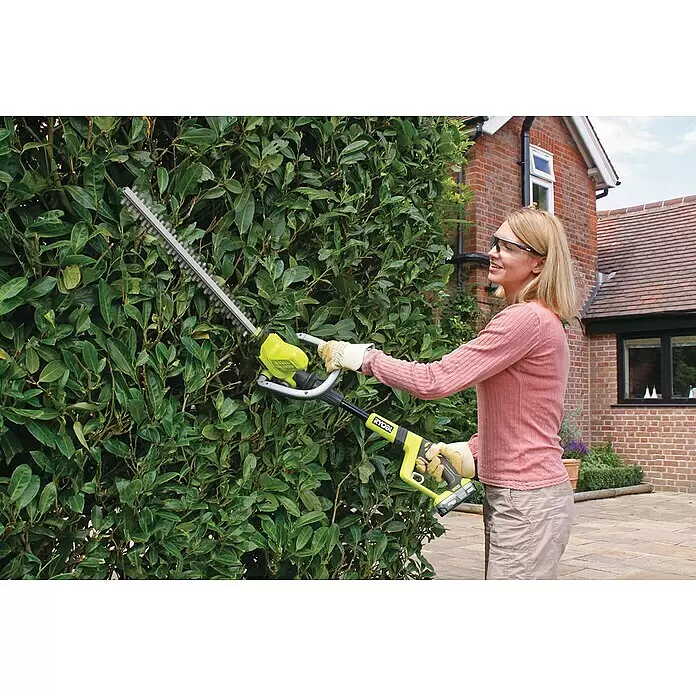 Ryobi ONE+ Akku-Heckenschere OHT1850X - 18 V, Li-Ionen, Ohne Akku, Schnittlänge: 45 cm - Eine Frau mit Schutzbrille und Handschuhen benutzt eine gelb-schwarze Ryobi Heckenschere zum Schneiden einer grünen Hecke.