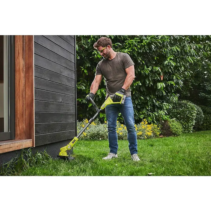 Ryobi ONE+ Akku-Rasentrimmer OLT1832 - 18 V, Li-Ionen, Ohne Akku - Ein Mann trimmt mit einem Ryobi Akku-Rasentrimmer den Rasen entlang einer dunklen Holzwand, umgeben von üppigem Grün.
