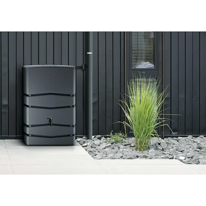 Regenspeicher Aqua Tower - L x B x H: 57,3 x 77,5 x 115 cm, 450 l, Anthrazit - Eine graue Regentonnen-Säule steht vor einer schwarzen Holzwand mit einem Fenster und Ziergras. Praktische Wasserspeicherung für den Garten.