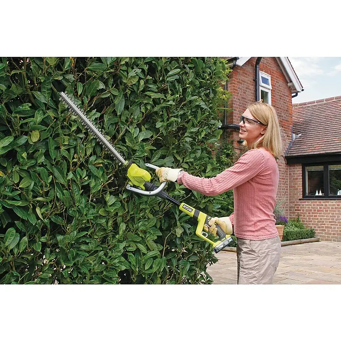 Ryobi ONE+ Maschinenpaket - Akku-Heckenschere OHT1850X,18V, 4 Ah Akku & 2A Ladegerät - Eine Frau schneidet eine Hecke mit einer Ryobi Heckenschere. Die Heckenschere ist gelb, schwarz und silber. Sie trägt Schutzkleidung.