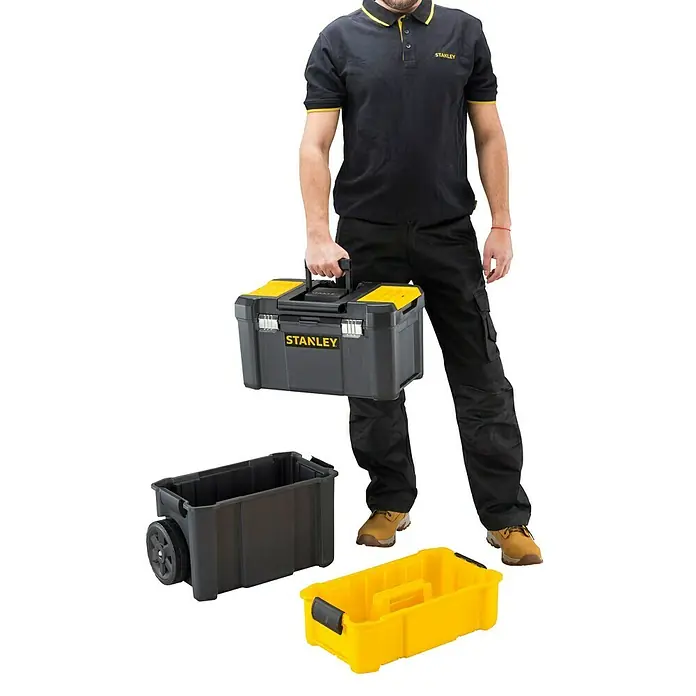 Stanley Rollende Profi-Box - Ohne Werkzeug, L x B x H: 47,5 x 28,5 x 62,3 cm - Das Bild zeigt einen Mann mit einer Stanley Werkzeugkiste und zwei weiteren Behältern. Die Werkzeugkiste ist grau mit gelben Akzenten.