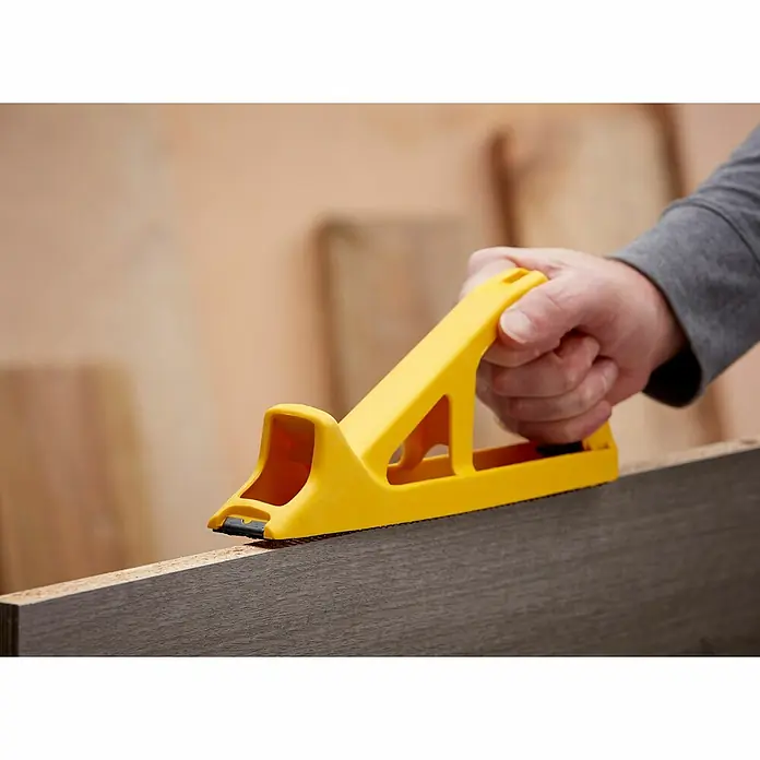 Stanley Blockhobel Surform - Kunststoff, Länge: 270 mm - Ein gelber Kantenhobel wird auf einem Holzbrett verwendet, um Kanten zu bearbeiten. Ein Werkzeug für präzise Holzbearbeitung.