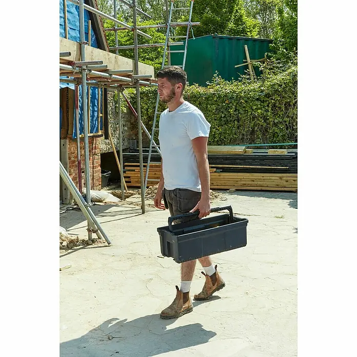 Stanley FatMax Werkzeugkasten FMST81083-1 - L x B x H: 29,6 x 64 x 28,7 cm, Klappbar - Ein Bauarbeiter trägt eine Werkzeugkiste auf einer Baustelle. Robuste Arbeitskleidung und Werkzeugbox für den täglichen Einsatz.