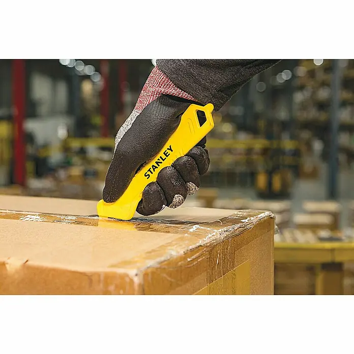 Stanley Sicherheitsmesser Light STHT10355-1Gebogen, 165 mm - Stanley-Kartonschneider im Einsatz: Gelber Schneider öffnet Karton in Lagerhalle, Schutzhandschuhe im Bild.