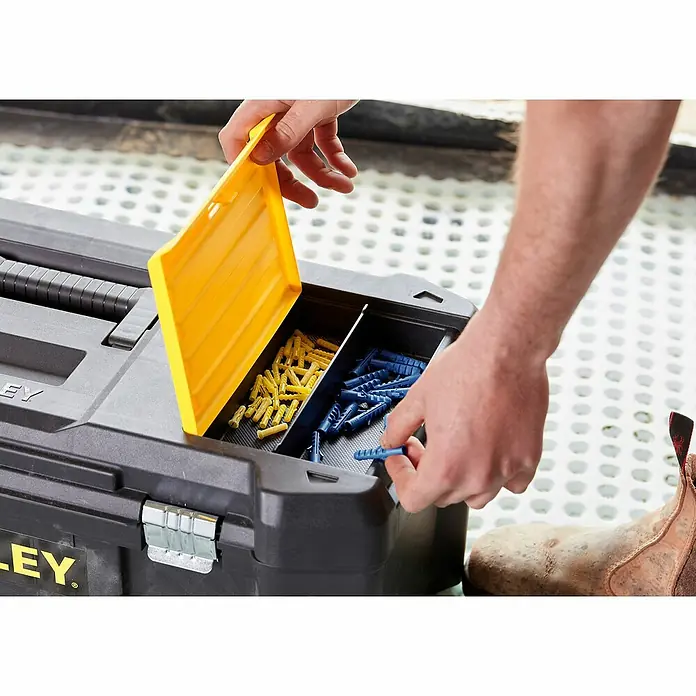 Stanley Werkzeugkasten ESSENTIAL™ STST82976-1 - B x L: 67 x 28 cm, Kunststoff - Nahaufnahme eines Stanley Werkzeugkastens mit gelben und blauen Dübeln, der von einer Hand geöffnet wird.\n
