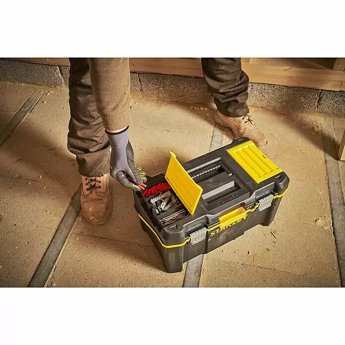 Stanley Werkzeugkasten ESSENTIAL™ Multi-Level Cantilever STST83397-1 - L x B x H: 25 x 49 x 29 cm, 19″, Kunststoff - Person in Arbeitskleidung entnimmt rote Dübel aus einer offenen, schwarz-gelben Stanley Werkzeugkiste mit Befestigungsmaterial auf Betonboden.