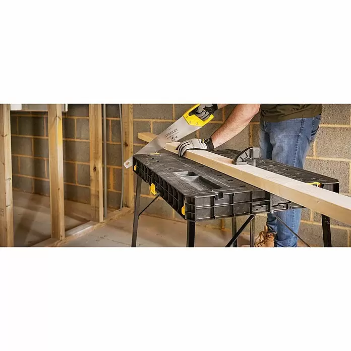 Stanley Werkbank ESSENTAIL™ STST83492-1 - L x B: 85 x 61 cm, Arbeitshöhe: 80 cm, Belastbarkeit: 320 kg, Schwarz/Gelb - Person sägt ein Holzbrett mit einer Stanley Handsäge auf einer schwarzen und gelben Stanley Werkbank.