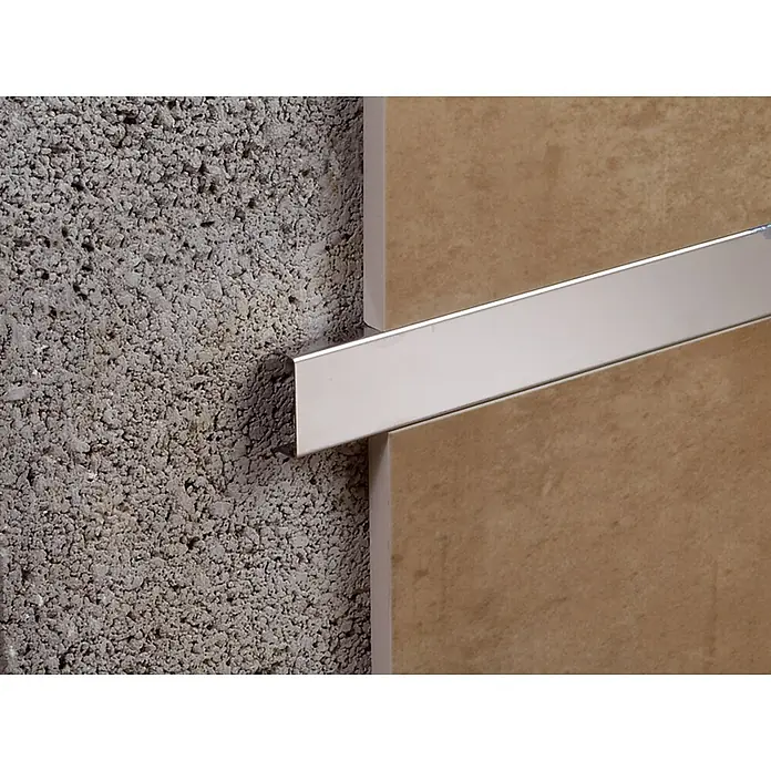 Perfil en U decorativo - Acero inoxidable, Acero inoxidable, 2,5 m x 8 mm - Primer plano de un borde de baldosa plateado, fijado a una pared de hormigón poroso y baldosas de color marrón claro. Ideal para un acabado limpio.