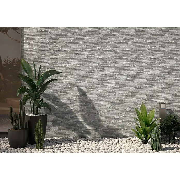 Revestimiento de pared Maule - 17 x 52 cm, Blanco, Mate - Pared gris con textura horizontal y plantas delante sobre piedras blancas. Decoración elegante y moderna.