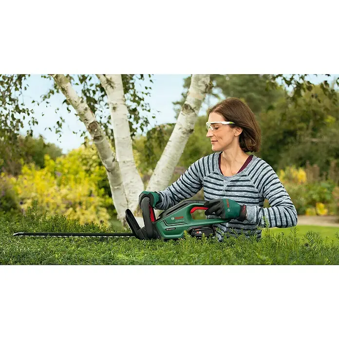 Bosch Power for All 18V Akku-Heckenschere UniversalHedgeCut 18V-50 - 2,5 V, Li-Ionen, Ohne Akku, Schnittlänge: 50 cm - Frau schneidet Hecke mit Bosch AdvancedHedgeCut 36V-65 Akku-Heckenschere, Schutzbrille und Handschuhe. Müheloses Trimmen mit der leistungsstarken Heckenschere.