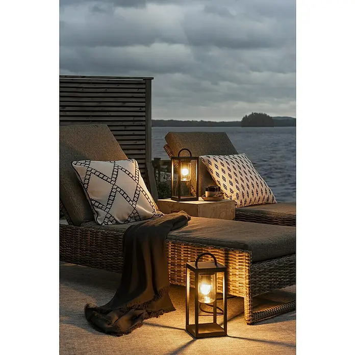 Konstsmide Metall-Laterne Bologna - 14 x 14 x 33 cm, Schwarz - Elegante Outdoor-Szene mit zwei Lounge-Liegen, dekoriert mit Kissen und Decke, beleuchtet durch stilvolle Laternen für eine gemütliche Atmosphäre.