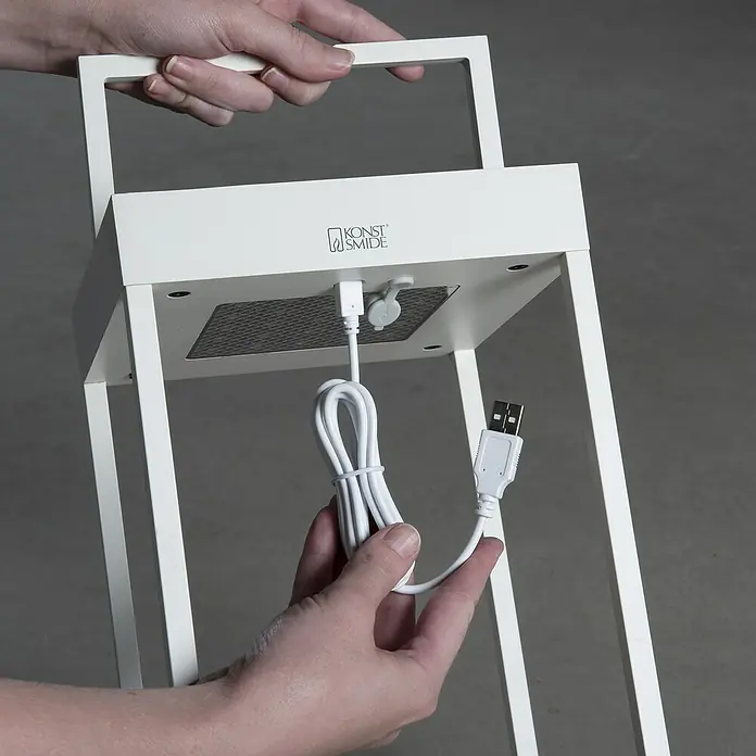 Konstsmide Außenlaterne Portofino - 15,5 x 18,5 x 30 mm, Weiß - Weiße Laterne mit USB-Kabel und Tragegriff, gehalten von Händen. Das moderne Design macht die Lampe zu einem dekorativen Lichtelement.