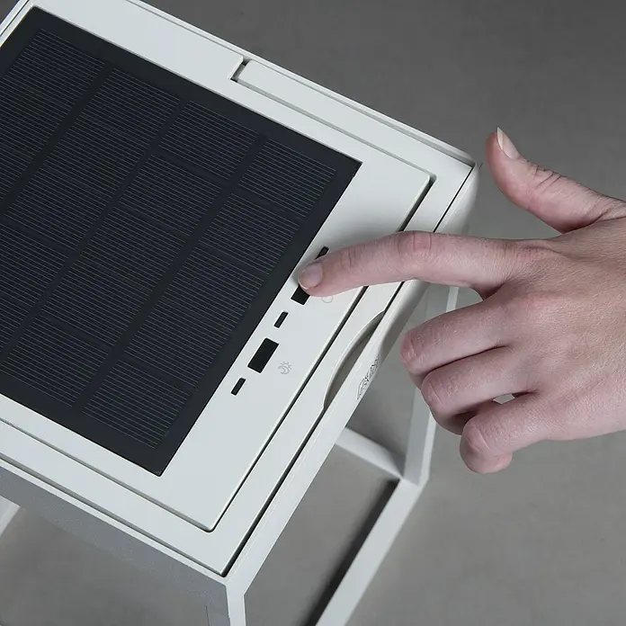 Konstsmide Außenlaterne Portofino - 15,5 x 18,5 x 30 mm, Weiß - Detailaufnahme einer Hand, die den Netzschalter eines tragbaren Solarpanels auf einem weißen Tisch betätigt.