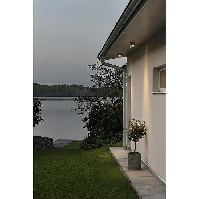 Konstsmide LED-Deckenleuchte Varese - Farbe Gehäuse: Anthrazit, IP54 - Außenansicht eines Hauses mit Außenbeleuchtung, die die Fassade erhellt und eine einladende Atmosphäre schafft.