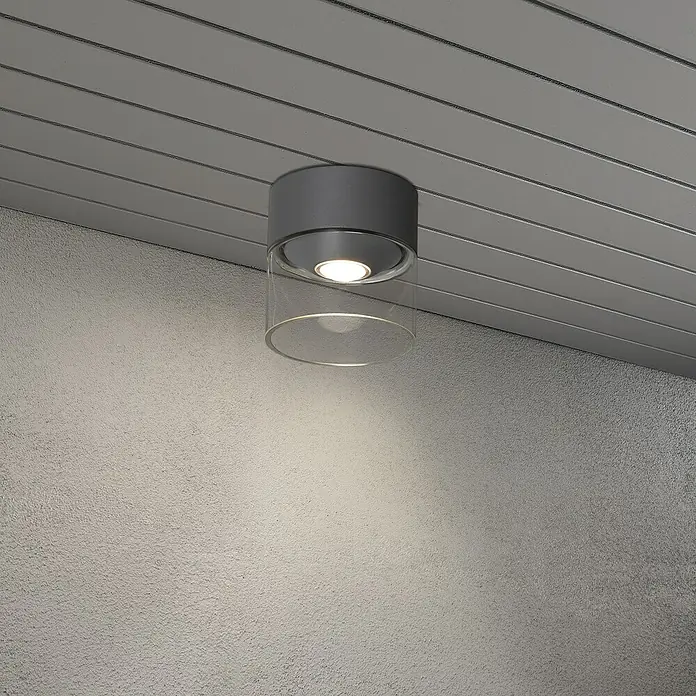 Konstsmide LED-Deckenleuchte Varese - Farbe Gehäuse: Anthrazit, IP54 - Nahaufnahme einer modernen grauen Deckenleuchte mit klarem Glasdiffusor, die ein warmes Licht in den Raum wirft. Perfekt für stilvolle Innenräume.