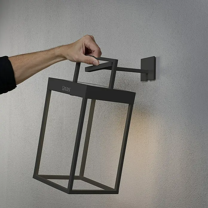 Konstsmide Außenlaterne Portofino - 15,5 x 18,5 x 30 cm, Schwarz - Schwarze, moderne Wandleuchte mit rechteckigem Design. Die Lampe wird von einer Hand gehalten und strahlt warmes Licht aus.