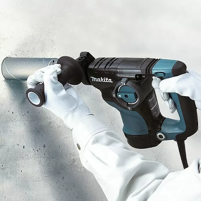 Makita Martillo combinado HR2811FT - 800 W, 2,8 J, Portabrocas de sujeción rápida - Un taladro percutor Makita negro y turquesa sostenido por manos enguantadas, perforando una pared de hormigón.
