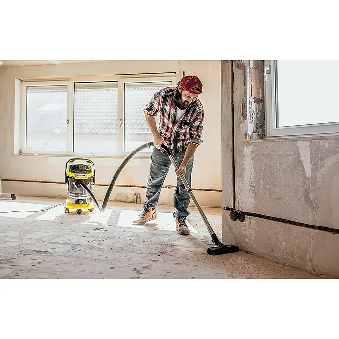Kärcher Elektro-Nass- & Trockensauger WD6 P S V-30/6/22/T - 1.300 W, Behältervolumen: 30 l - Mann reinigt mit einem Kärcher Mehrzwecksauger einen Raum im Rohbau, um Staub und Schmutz zu beseitigen. Das Gerät ist gelb und grau.
