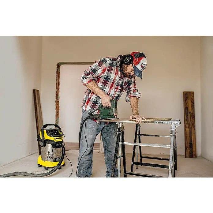 Kärcher Elektro-Nass- & Trockensauger WD6 P S V-30/6/22/T - 1.300 W, Behältervolumen: 30 l - Ein Handwerker arbeitet mit einer Stichsäge an einem Holztisch, während ein Kärcher Staubsauger bereitsteht, um den Staub zu beseitigen.
