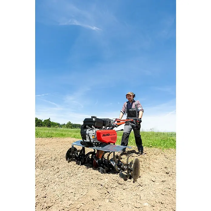 AL-KO Comfort Benzin-Bodenhacke MH 1150 Comfort - 3,6 kW, 4-Takt, Max. Flächenempfehlung: 670 m² - Ein Landwirt bedient eine AL-KO MH 1150 Motorhacke auf einem Acker. Die Maschine ist rot und schwarz und lockert den Boden für die Aussaat.
