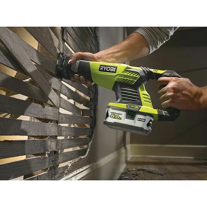Ryobi ONE+ Maschinen-Set Combo Kit R18CK4E-242S - 18 V, 2 Akkus, 8 -tlg. - Ein Mann benutzt eine Ryobi Akku-Säbelsäge, um eine Wand zu bearbeiten. Das Werkzeug ist grün und schwarz mit einem 5,0 Ah Akku.