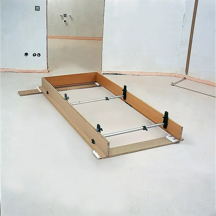 Bessey Türfuttermontagestrebe TMS - Spannweite: 560 mm - 1.010 mm - Ein rechteckiger Rahmen mit Metallstangen und schwarzen Klammern steht auf einem hellen Boden in einem unfertigen Raum.