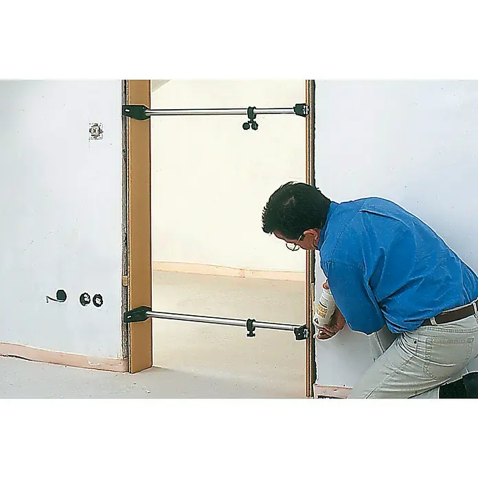 Bessey Türfuttermontagestrebe TMS - Spannweite: 560 mm - 1.010 mm - Ein Mann dichtet mit Schaum eine Tür ab, die mit einem Spreizer stabilisiert ist. Der Spreizer fixiert den Türrahmen.