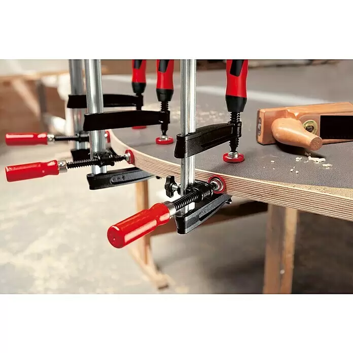 Bessey Kantenzwinge KT 5-1 CP - 1 Spindel - Mehrere Schraubzwingen mit roten Griffen und schwarzen Körpern fixieren eine gebogene Holzplatte an einer Werkbank.