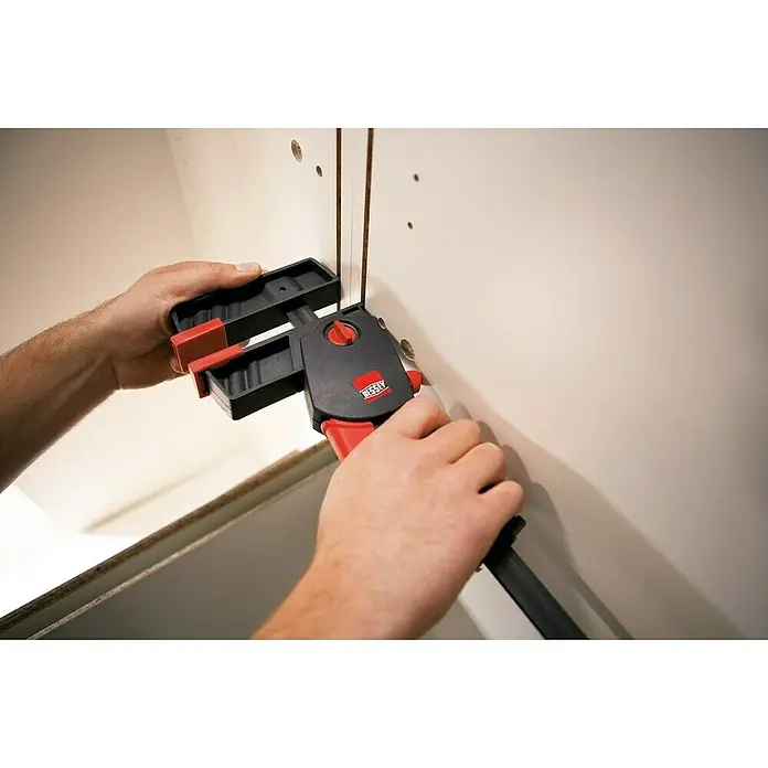 Bessey Einhandzwinge DuoKlamp DUO 30-8 - Spannweite: 300 mm, Spannkraft: 1.200 N, Ausladung: 85 mm - Eine Person befestigt mit einer Einhandzwinge von Bessey ein Werkstück. Die Zwinge ist schwarz-rot und wird zum Fixieren verwendet.