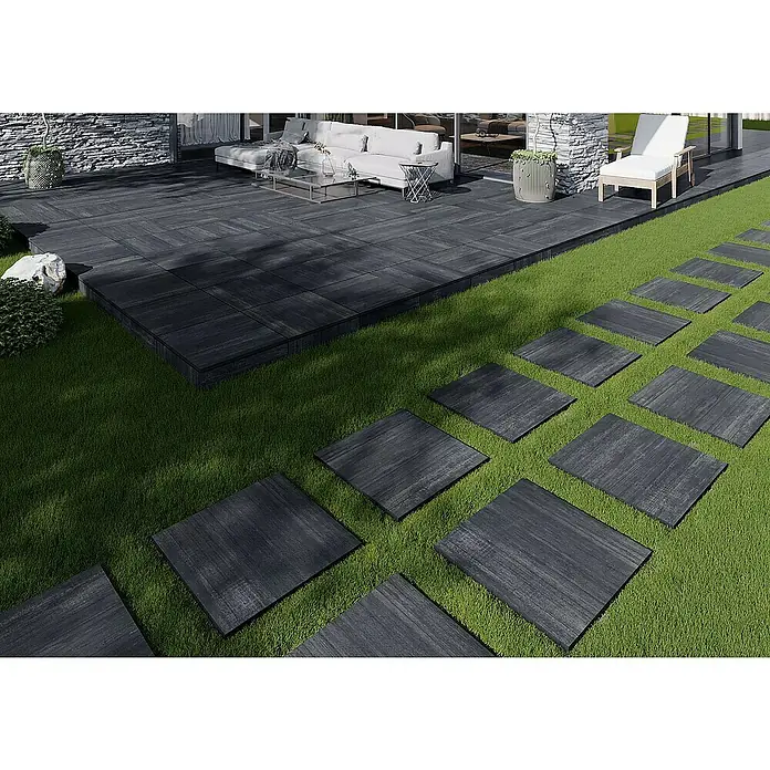 Terrassenfliese Garden Black Struktur - 59,7 x 59,7 x 2 cm, Schwarz, Matt - Ein stilvoller Außenbereich mit dunklen Terrassenplatten und einem Pfad aus Trittsteinen im grünen Rasen. Elegantes Design für Garten und Terrasse.