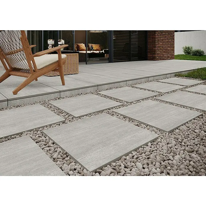 Terrassenfliese Garden Grey Struktur - 59,7 x 59,7 x 2 cm, Grau, Matt - Das Bild zeigt moderne Terrassenplatten in Grau, die mit kleinen Kieseln umrandet sind, wodurch ein stilvoller Außenbereich entsteht.