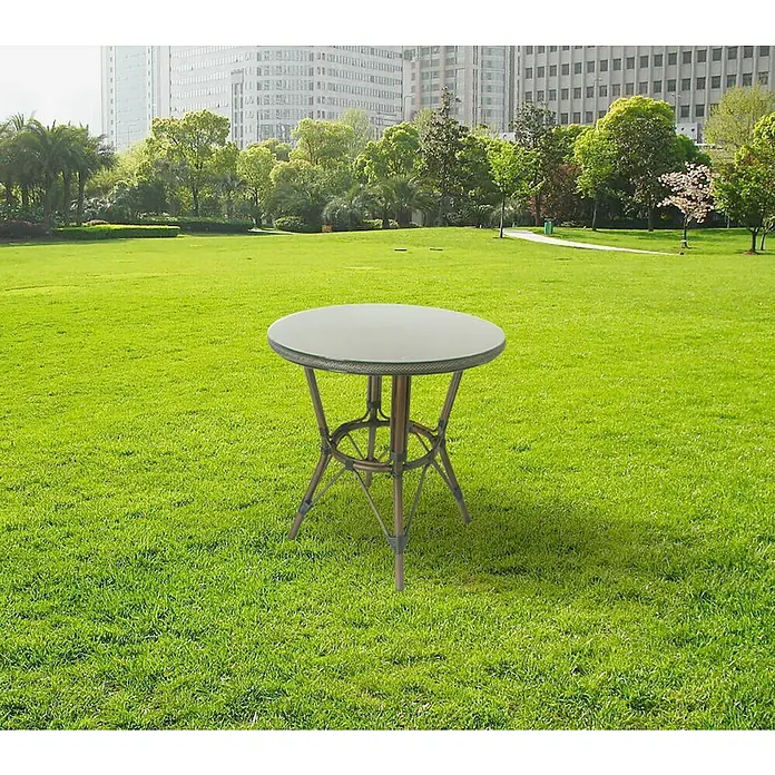 Mesa de jardín Sibuco - L x An x Al: 70 x 70 x 74 cm, Aluminio, Marrón oscuro - Una mesa redonda de patio con tapa de vidrio se encuentra en un césped verde, rodeado de árboles y edificios al fondo.