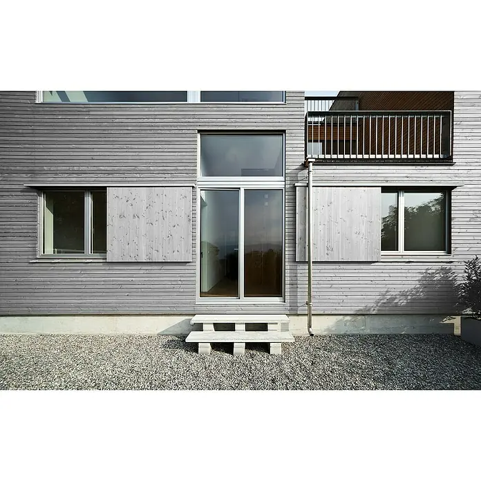 Fassaden-Profil Rhombus - Kiefer, L x B: 300 x 5,8 cm, Stärke: 2,8 cm, Grau - Das moderne Haus verfügt über Fenster mit hellgrauen Holzschiebeläden und eine minimalistische Steintreppe vor dem Eingang.
