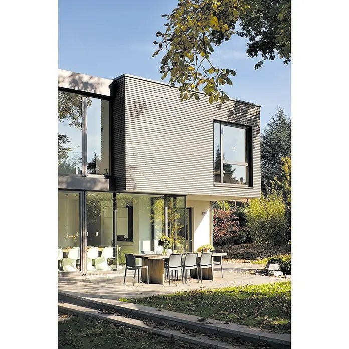 Unterkonstruktion - 300 x 7 x 4,5 cm, Kiefer - Moderne Hausfassade mit horizontaler Holzverkleidung, großen Fenstern und Essbereich im Freien mit stilvollen Stühlen.